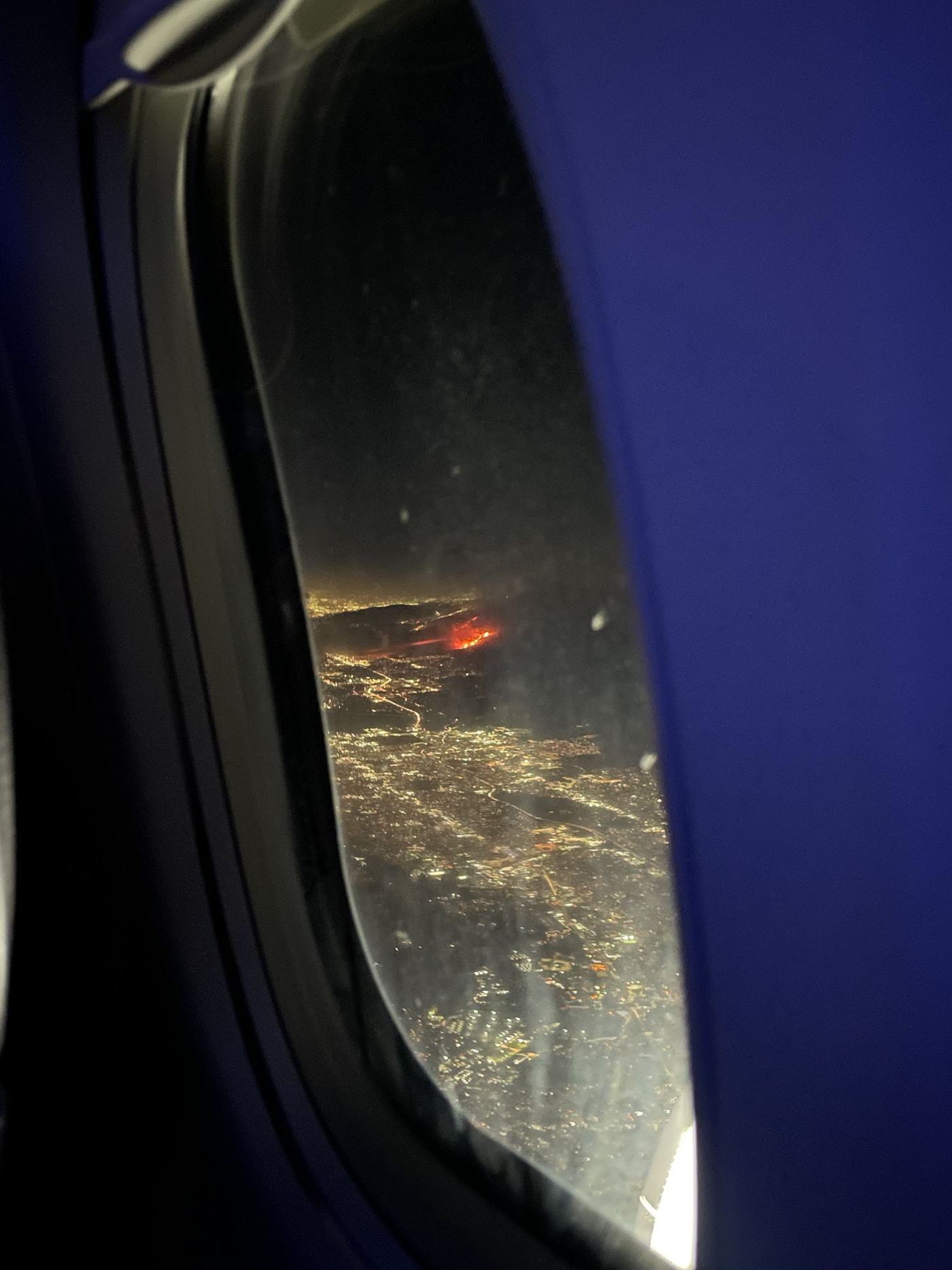 The Eaton Fire glowing red in the dark hills below a city grid of lights, seen from an airplane window at night.